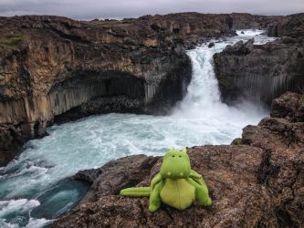 kleiner Drache Roloc sitzt vor einem Wasserfall in Island
